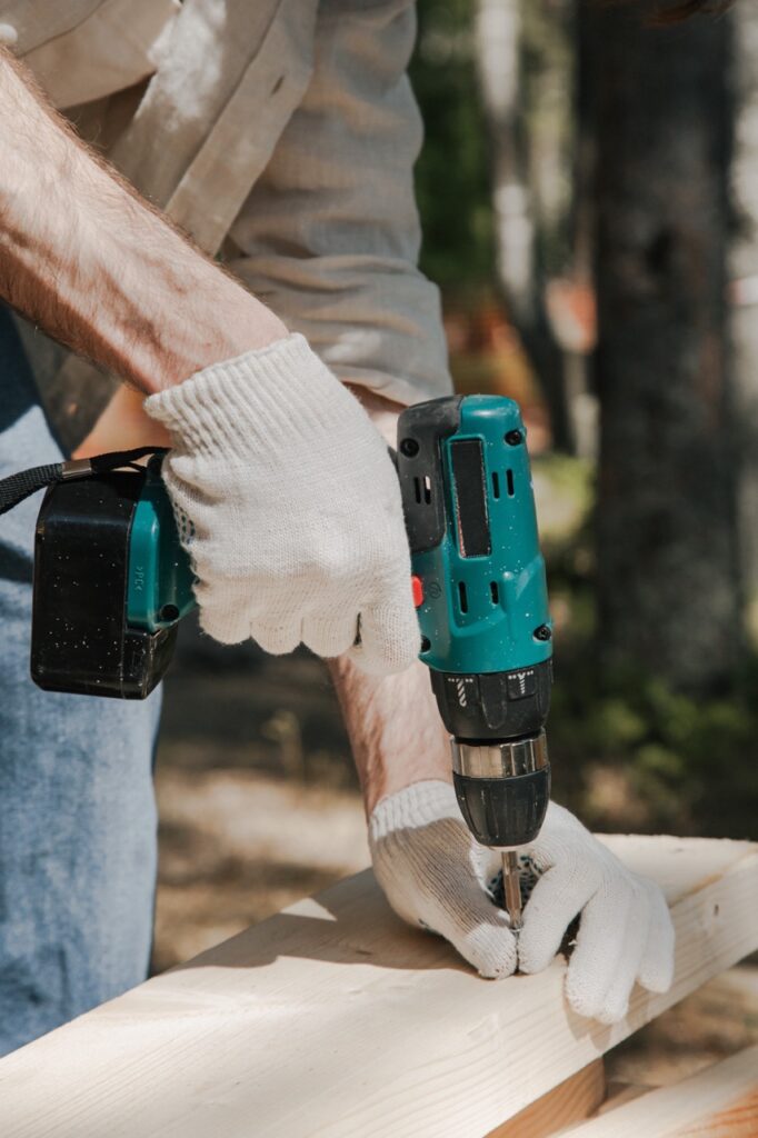 Man wearing gloves while using a power drill at a construction site.